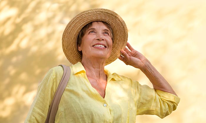 happy senior woman in sun hat walks on summer city against the