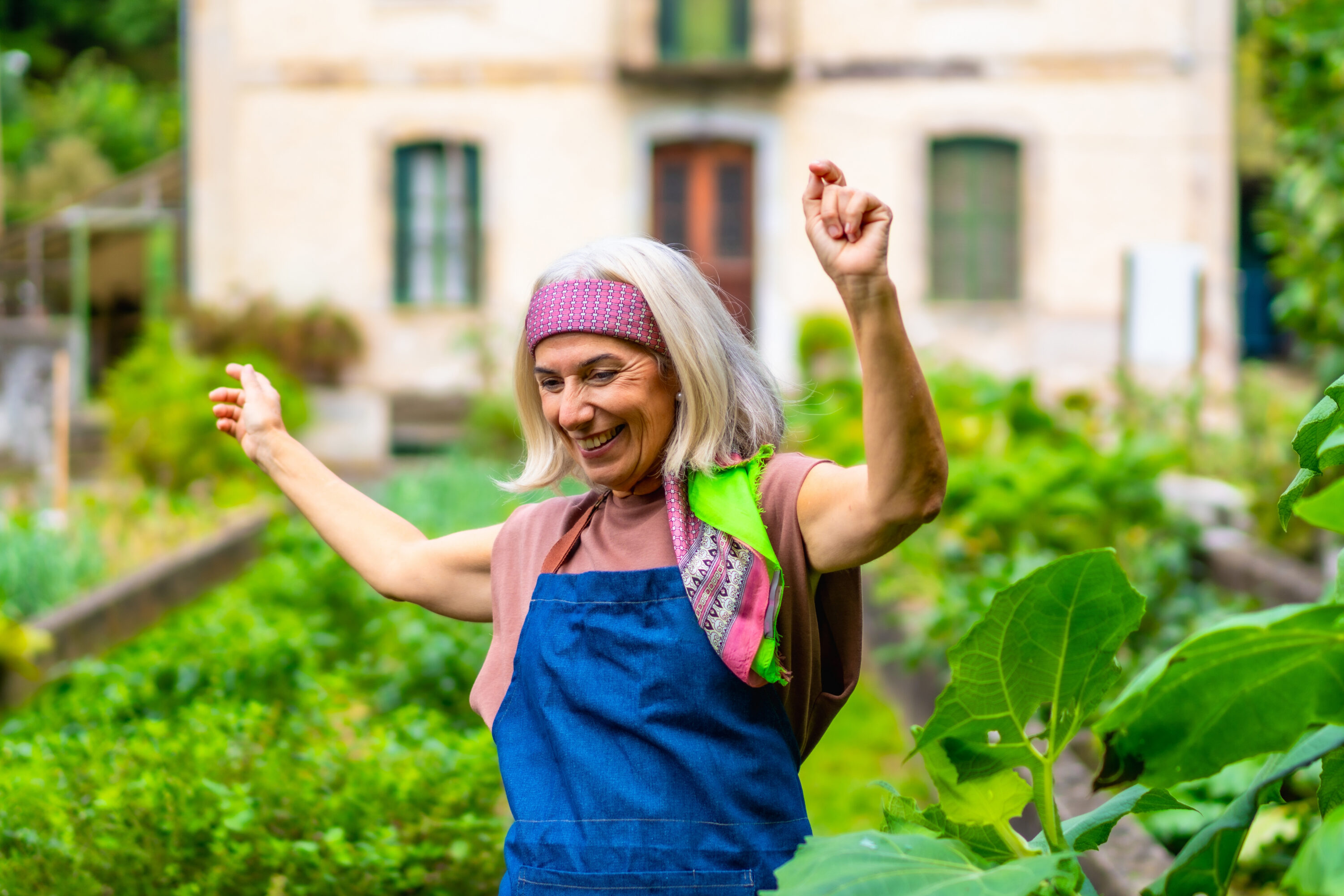 Smiling woman gardening with arms raised outdoors