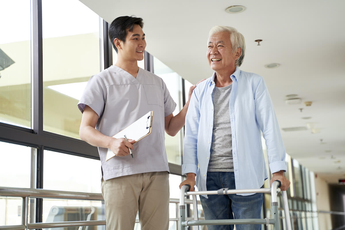 Nurse assisting elderly man with walker indoors