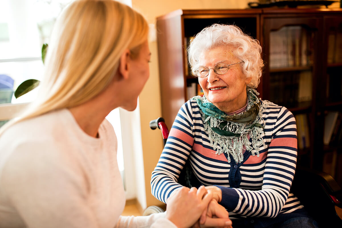 Caregiver holding elderly woman's hands at home