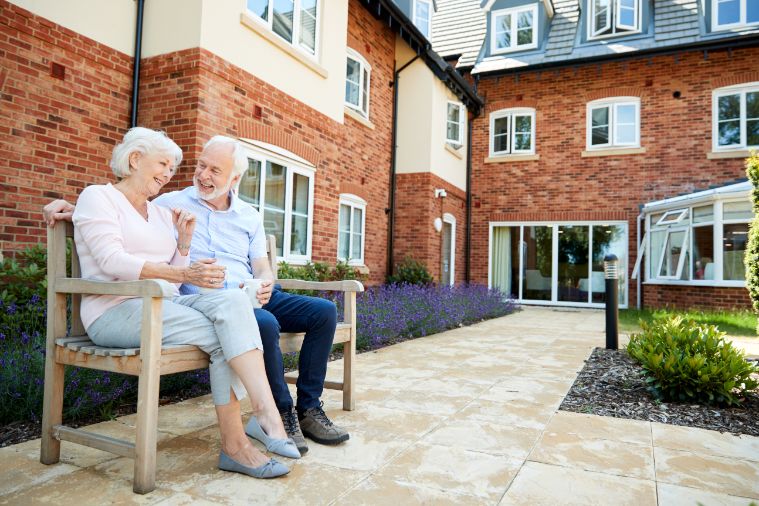 Elderly couple sitting on bench outside residence