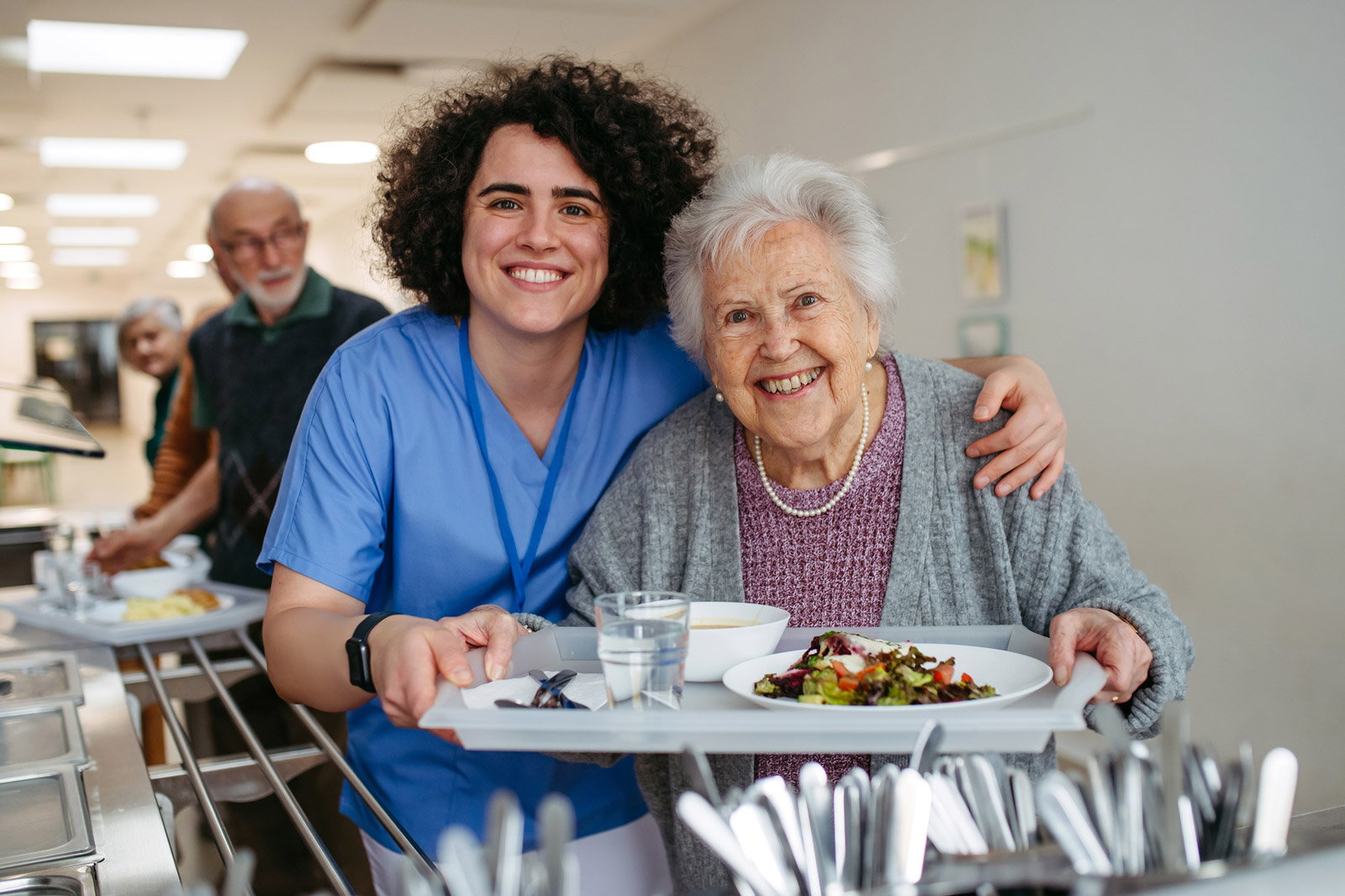 Caregiver and elderly woman holding meal tray