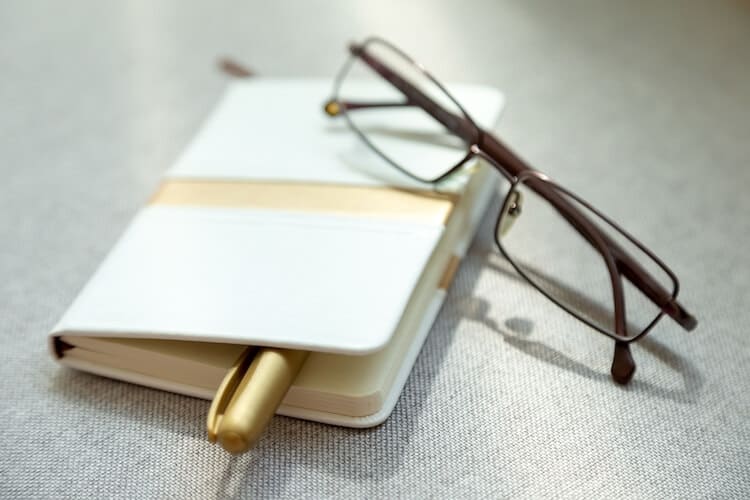 Eyeglasses resting on notebook with pen