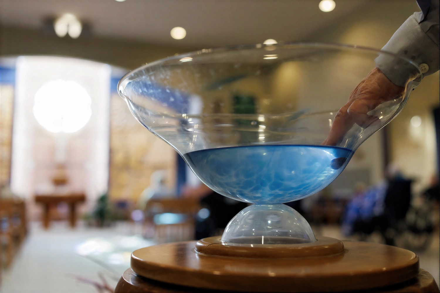 Hand touching blue water in baptismal font