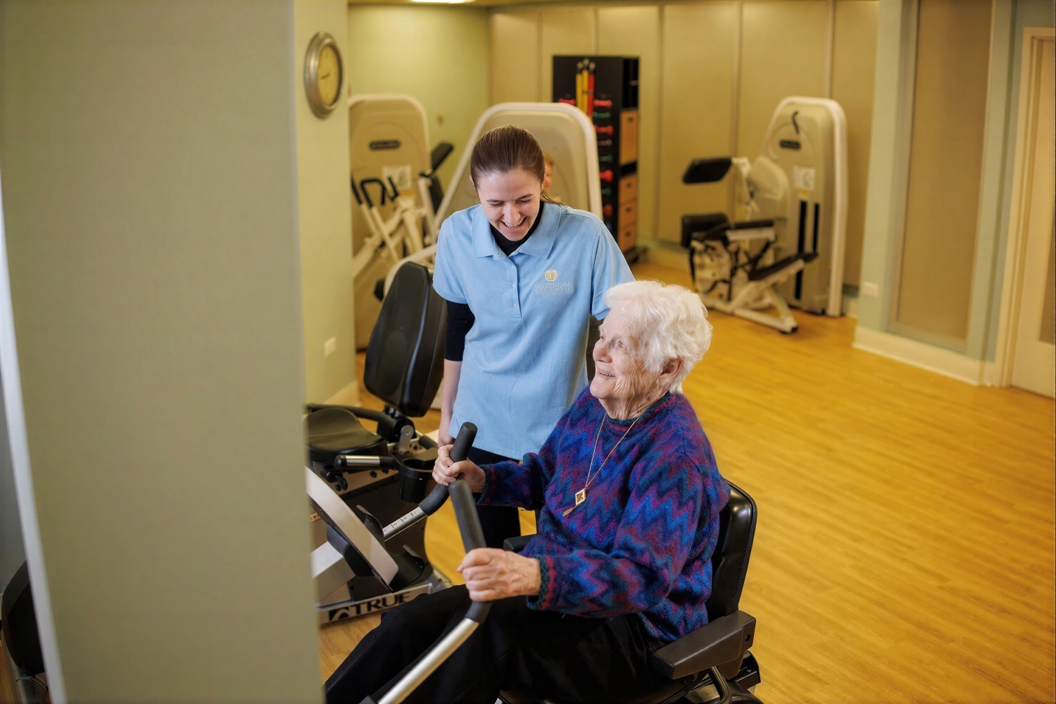 Elderly woman exercising with caregiver in rehab gym