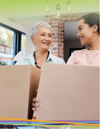 Two women holding moving boxes, smiling indoors