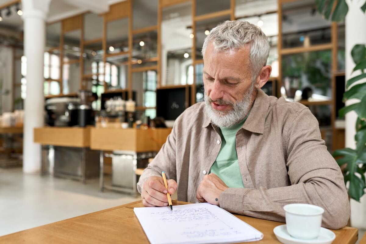 Gray-haired man writing at cafe table