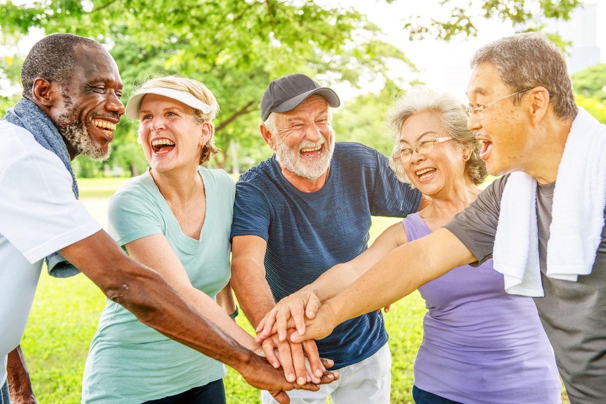 Group of seniors stacking hands outdoors smiling