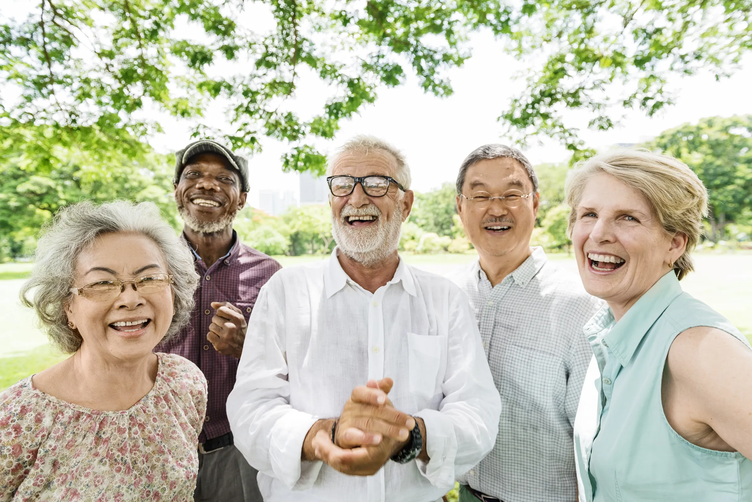 Five smiling seniors standing together in a park