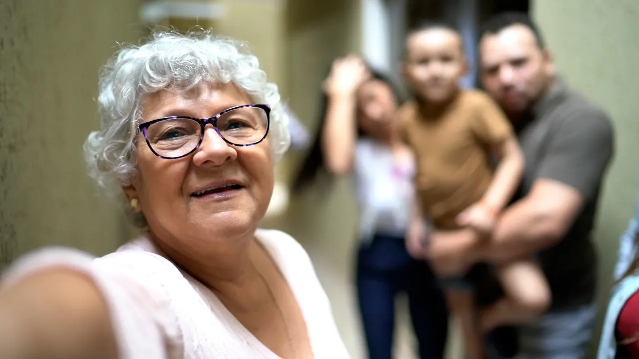 Smiling elderly woman taking selfie with family behind