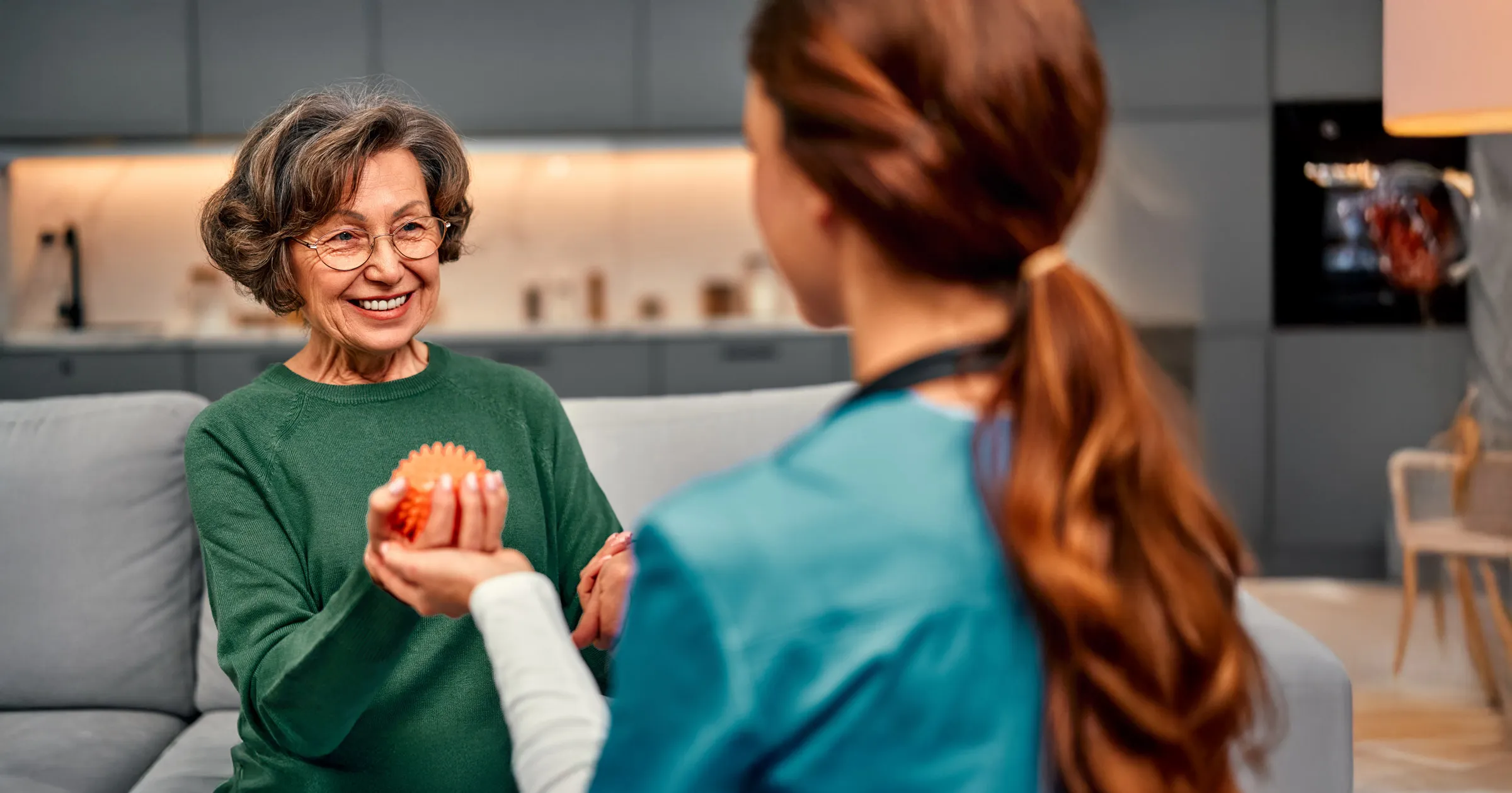 Elderly woman holding therapy ball with caregiver
