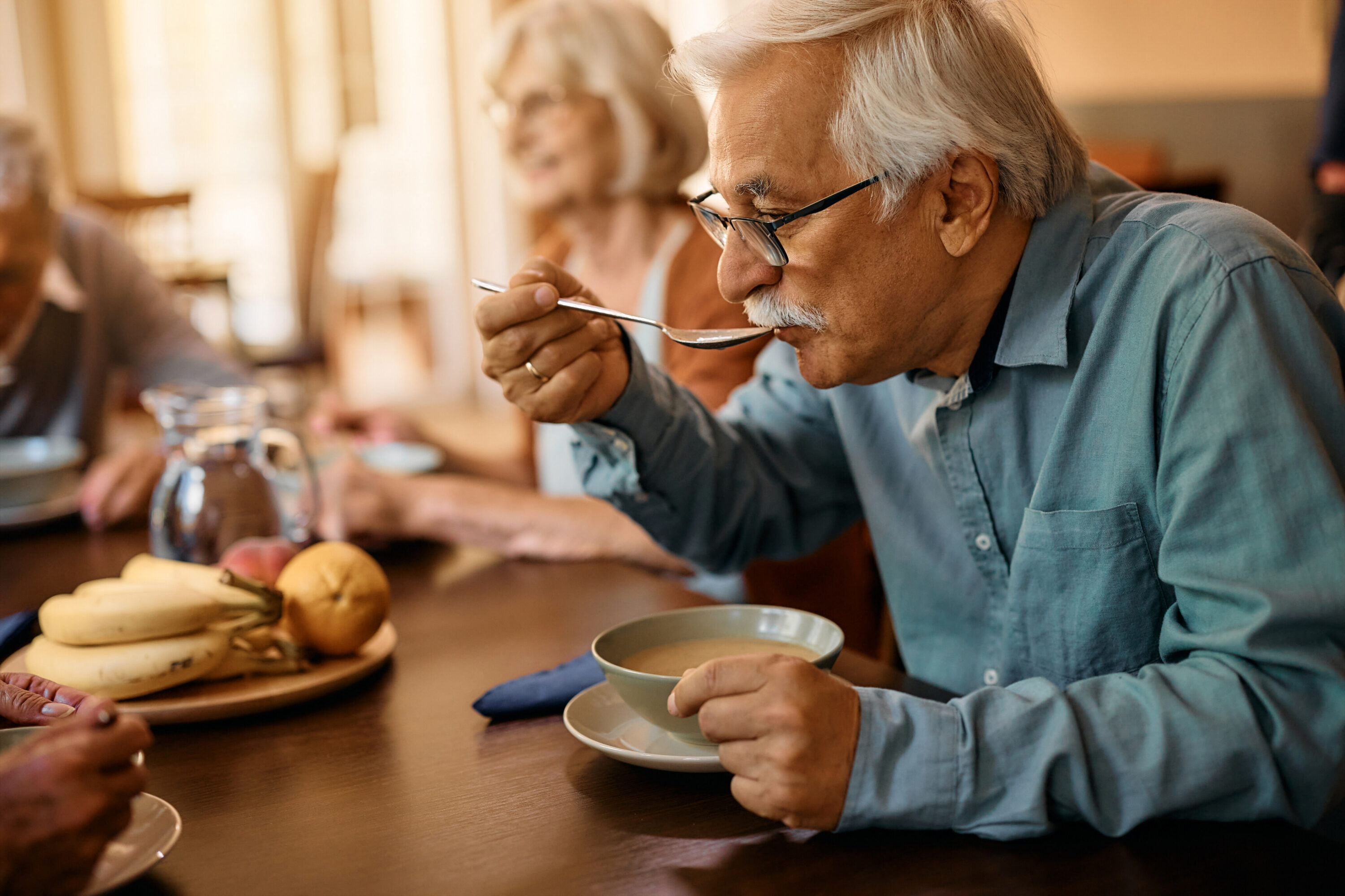 Elderly man eating soup at dining table