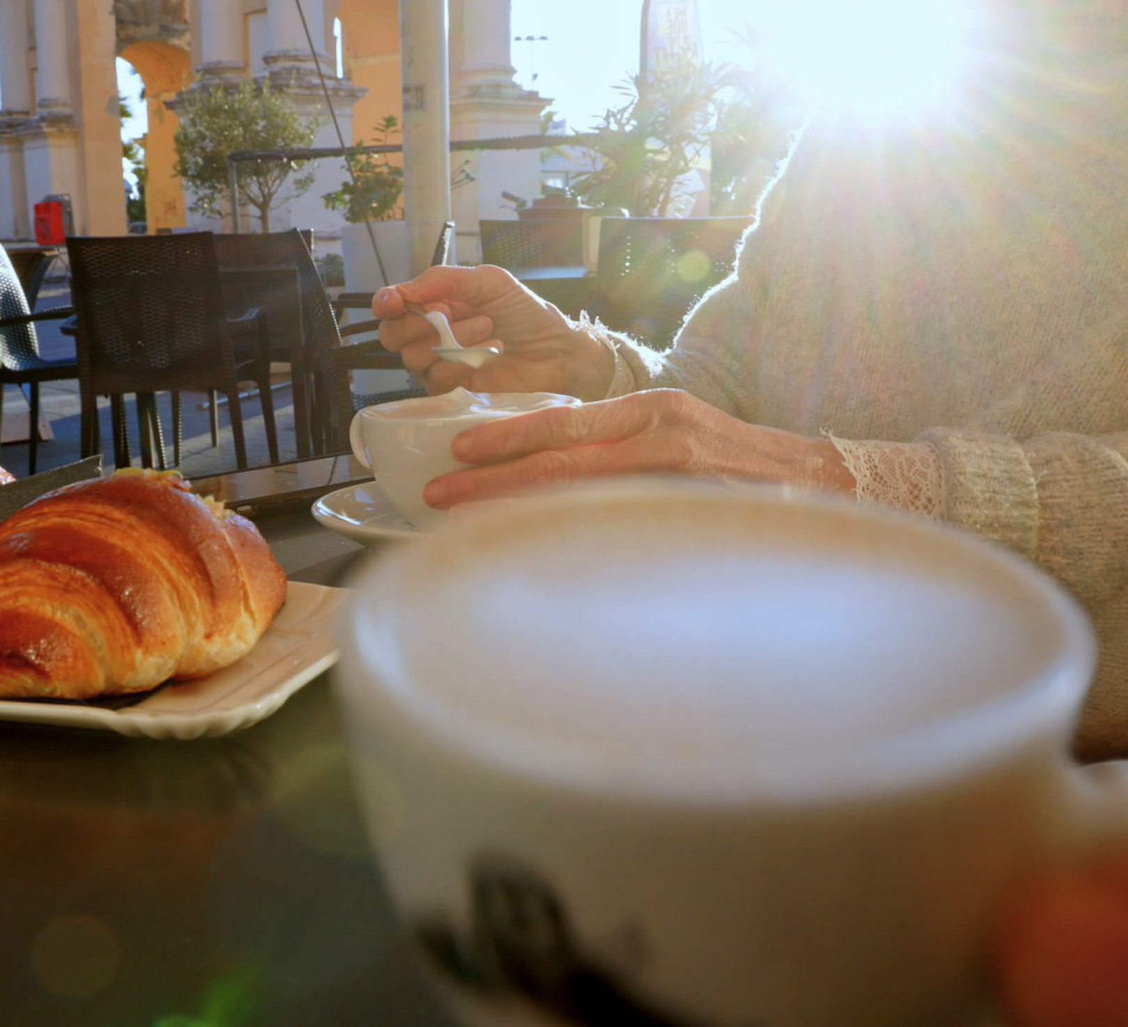 Person stirring coffee at sunny outdoor café