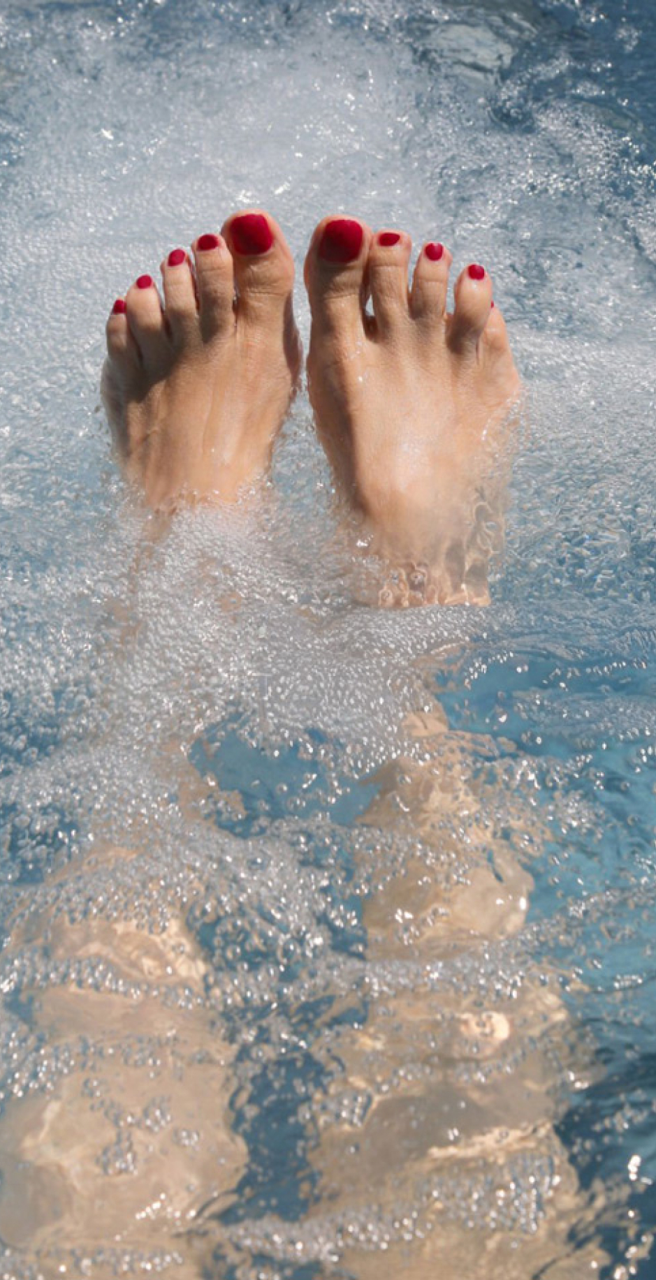 Feet with red toenails in bubbling water