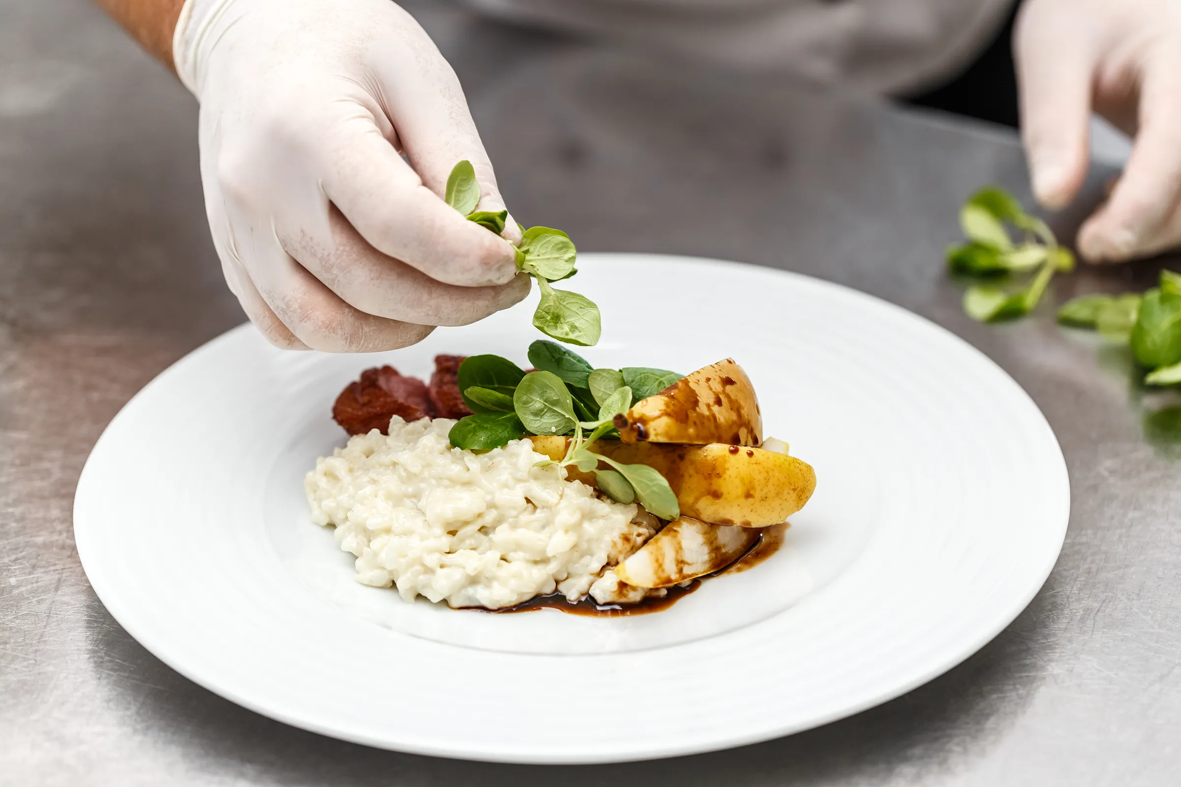 Chef garnishing risotto with pear and greens
