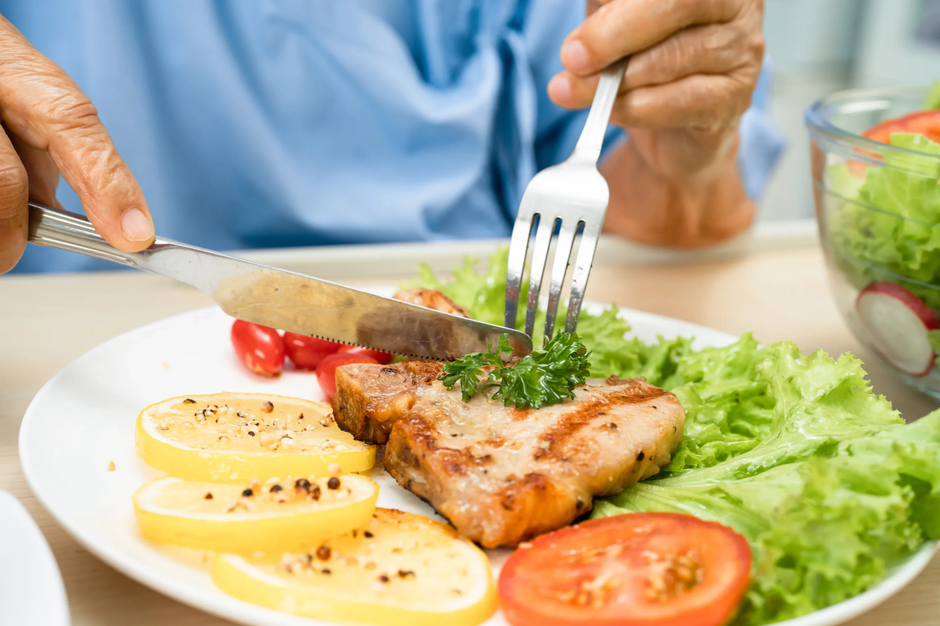 Person cutting grilled salmon with fresh vegetables
