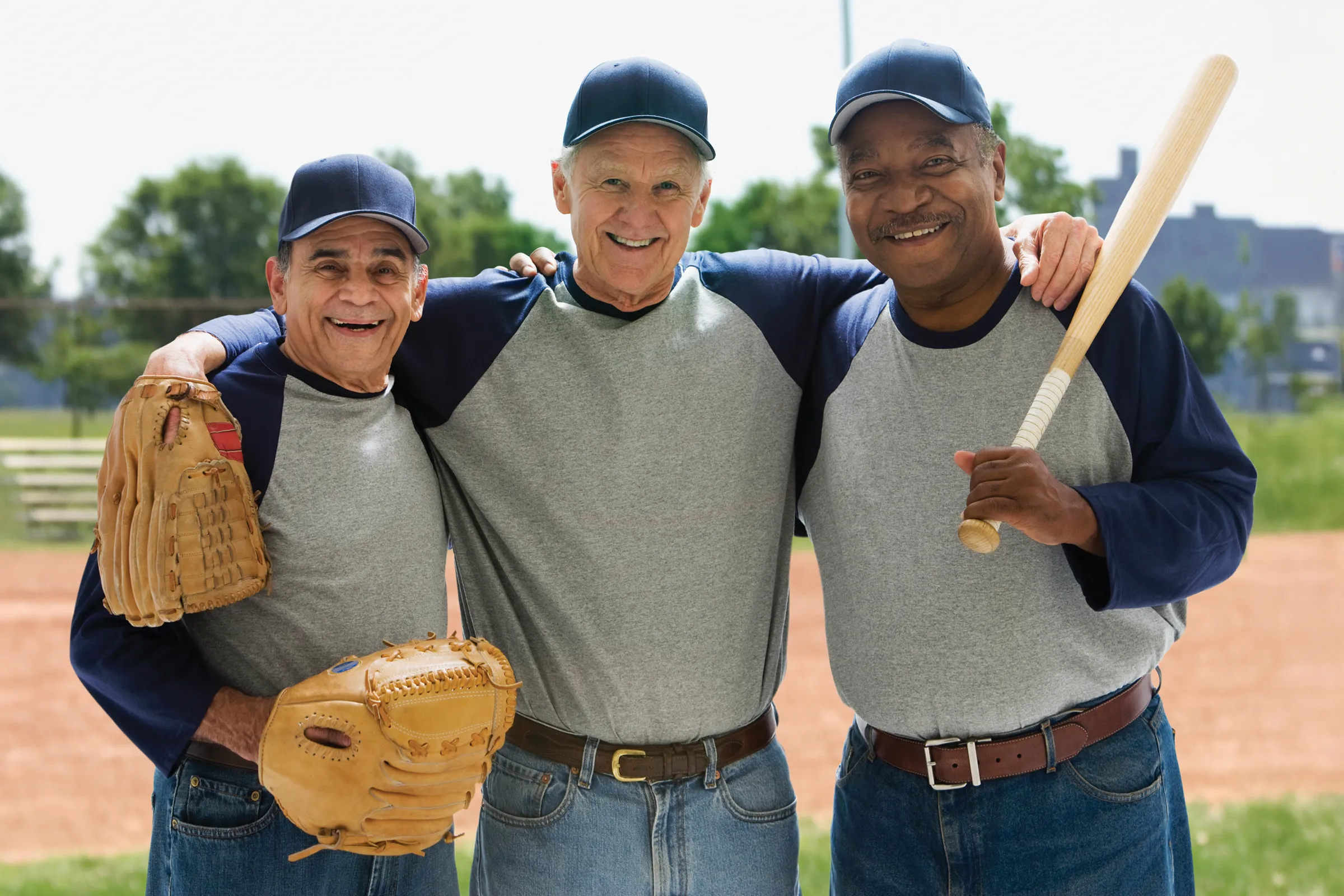 Three senior men in baseball uniforms smiling together