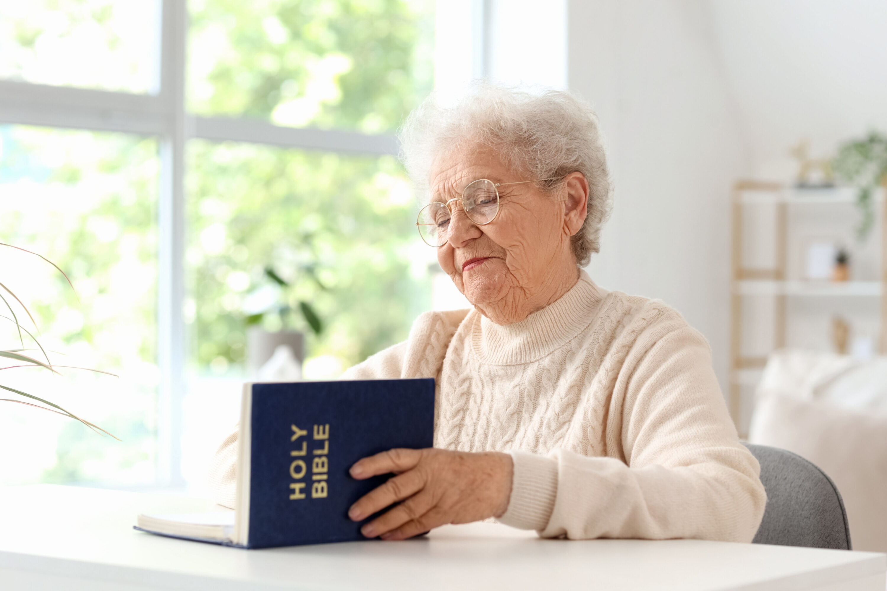 Elderly woman reading Holy Bible by window