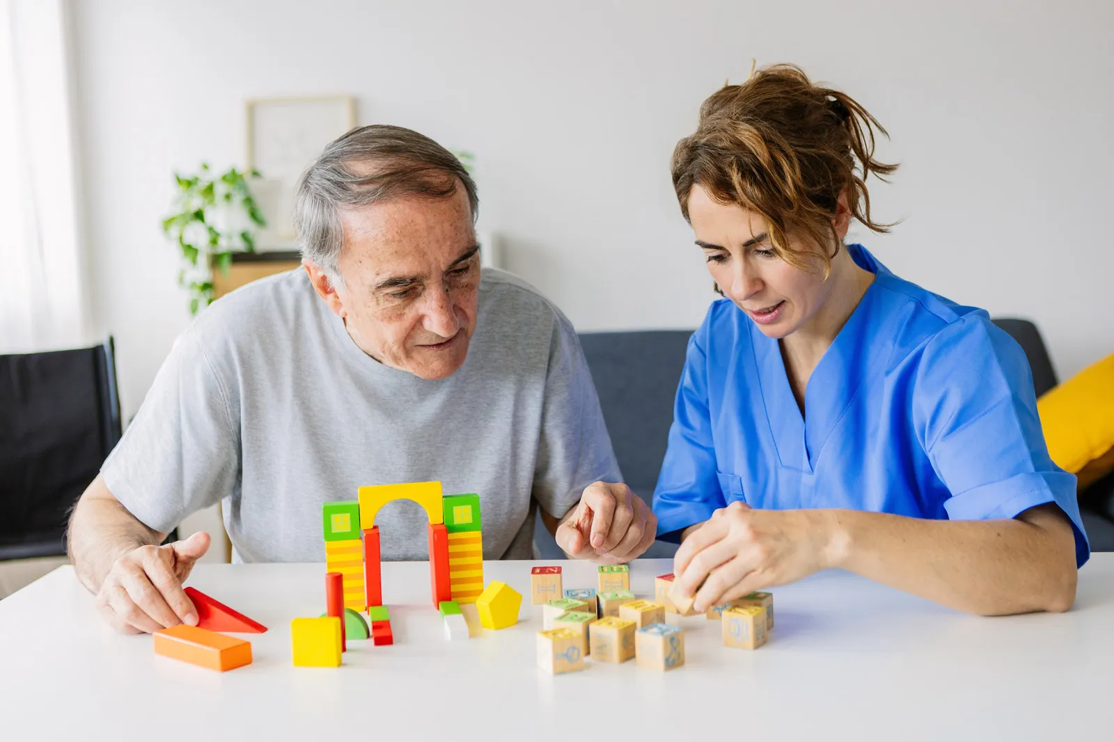 Caregiver assisting elderly man with colorful building blocks