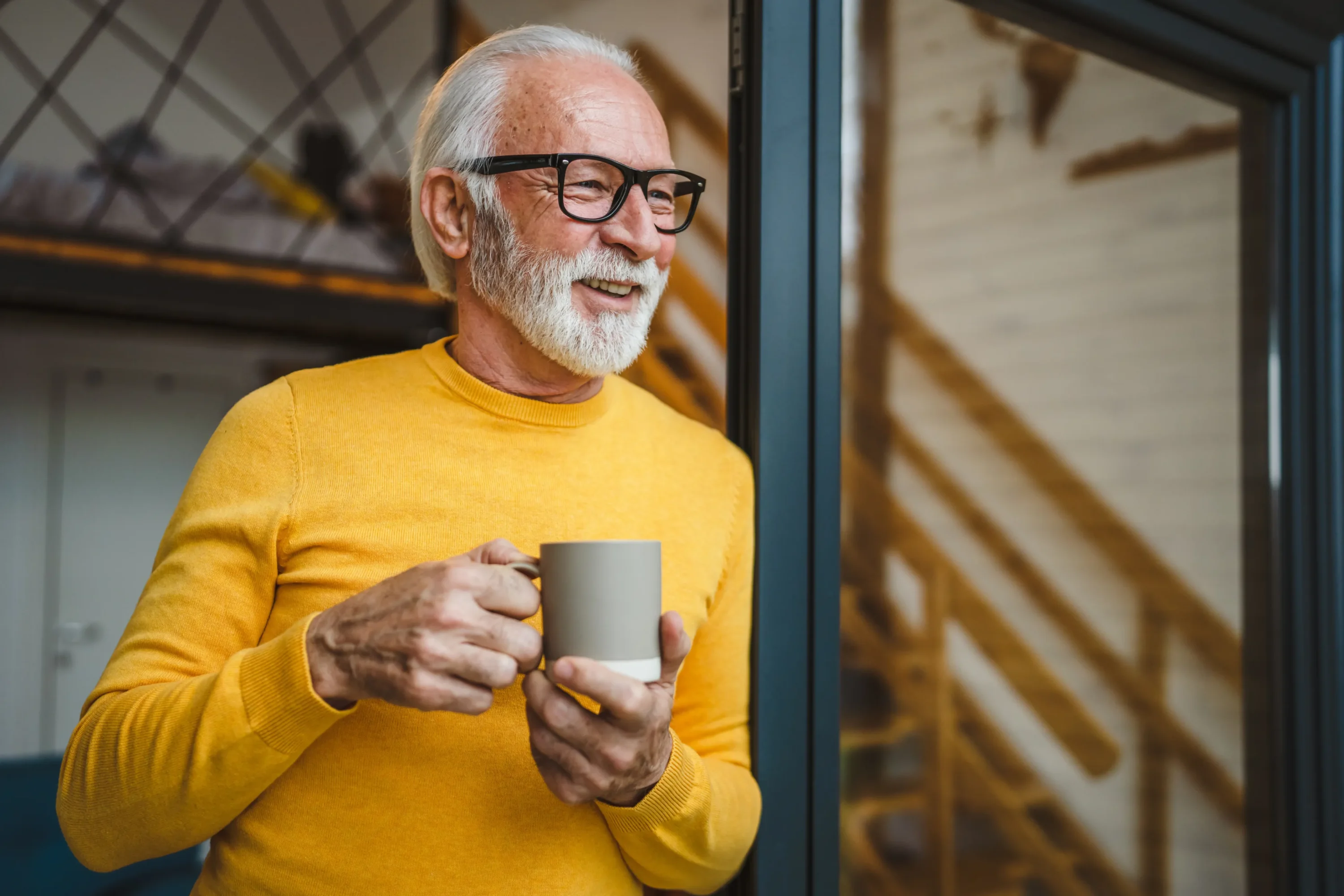 Smiling elderly man holding coffee mug by window