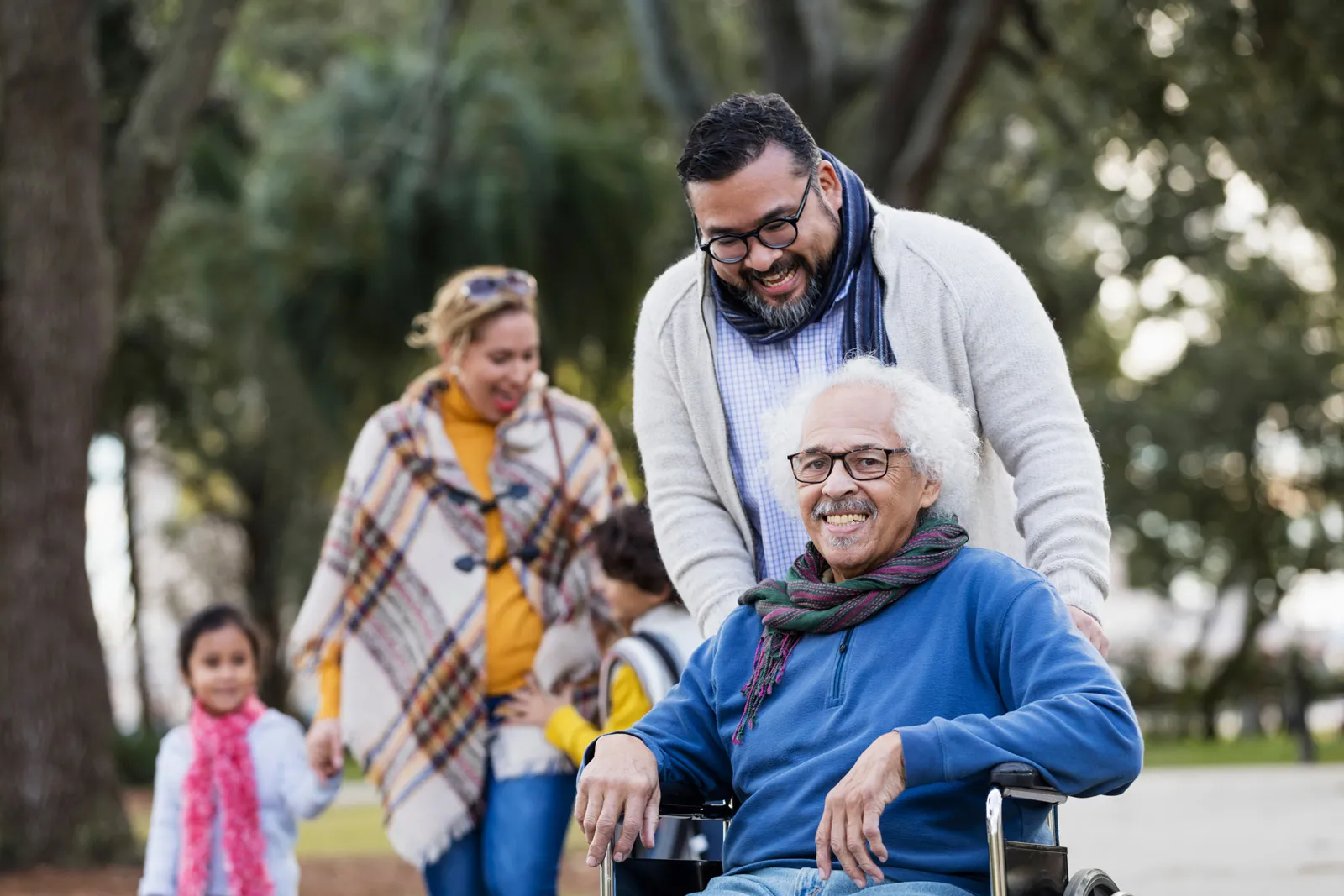 Family enjoying walk in park with grandfather in wheelchair