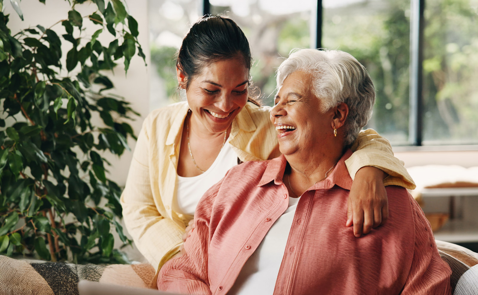 Adult daughter hugging laughing elderly mother indoors