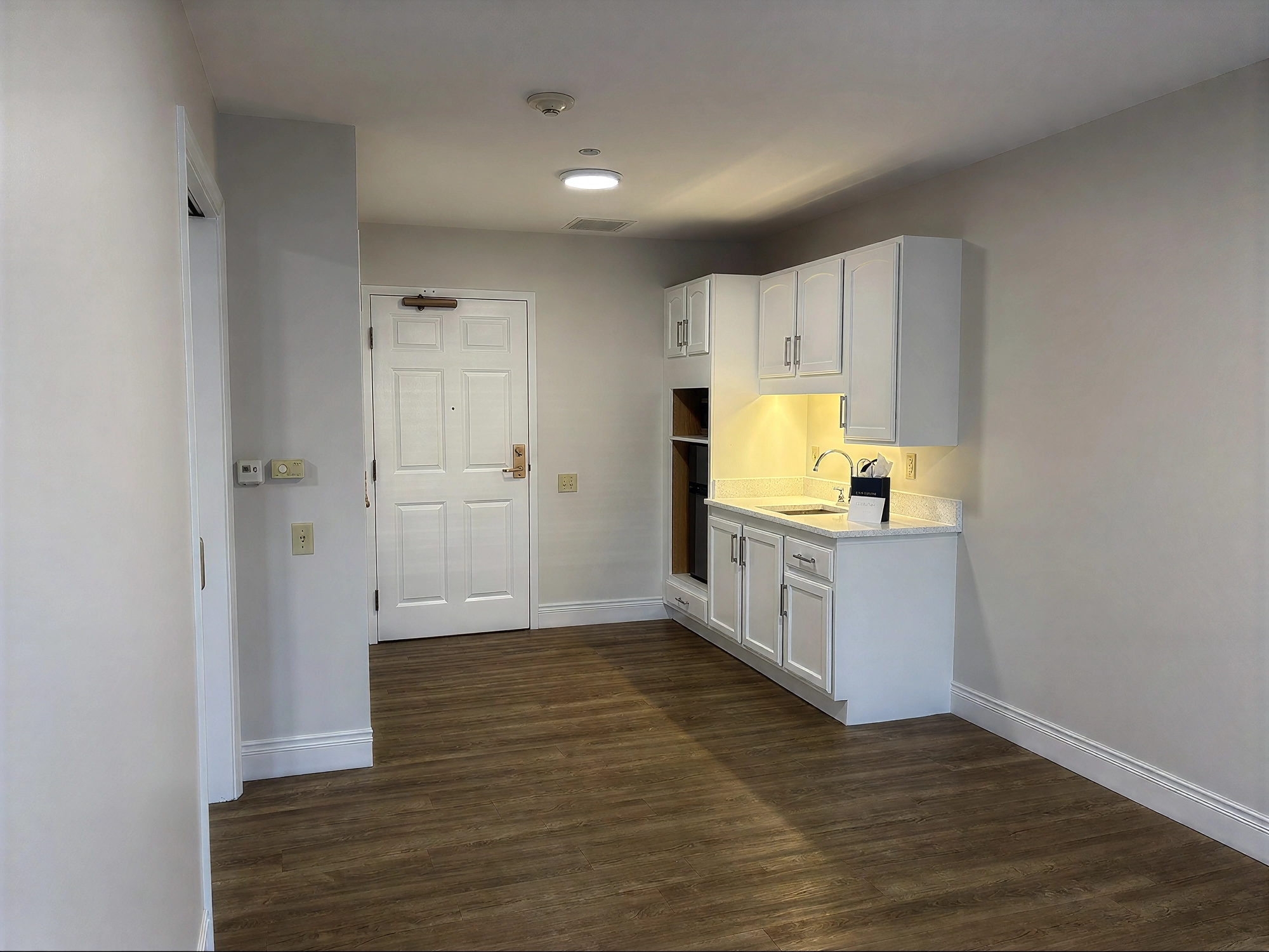 Small kitchenette with white cabinets and wood flooring
